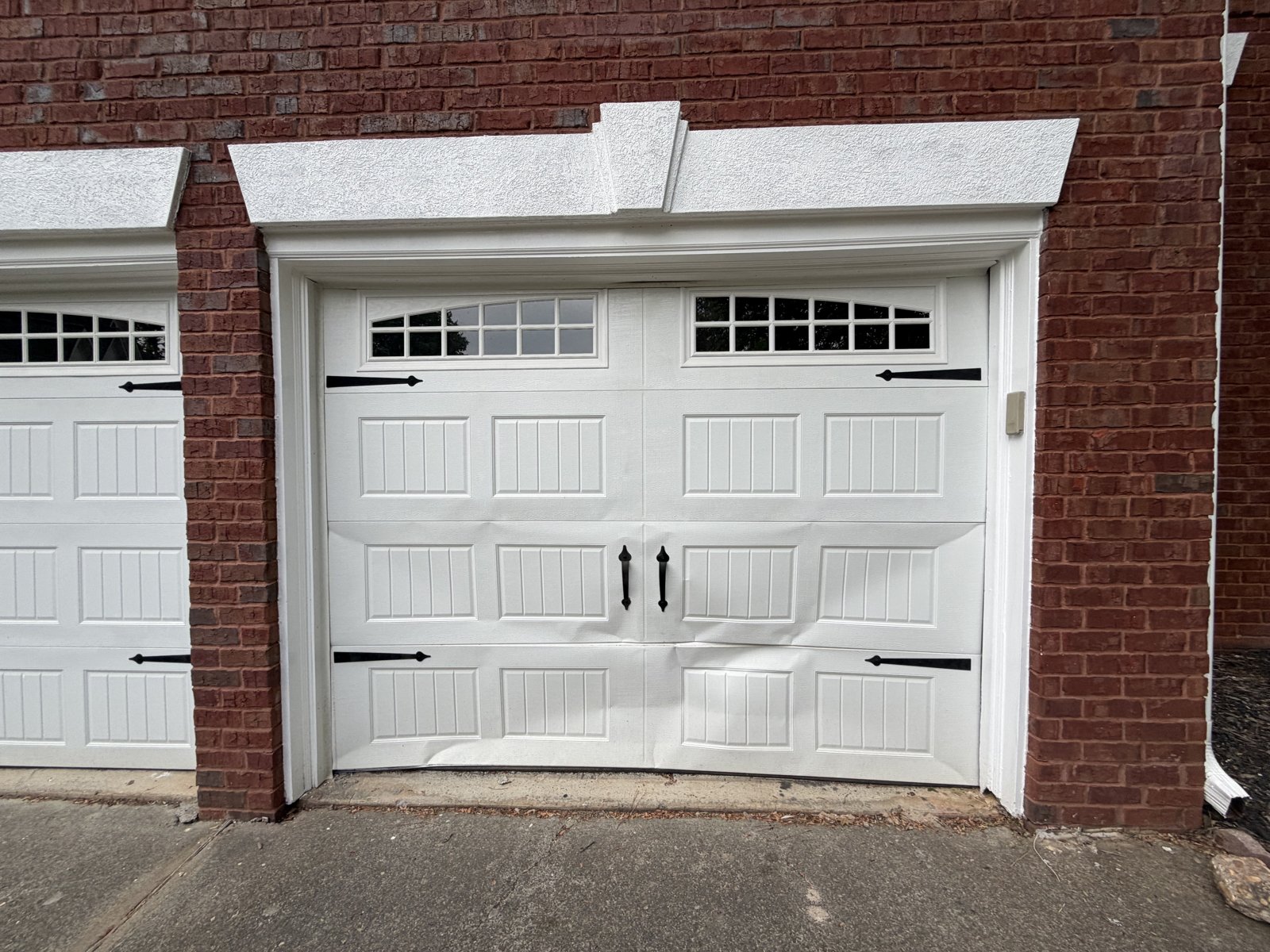 White carriage garage door with windows White carriage-style garage door with top windows and black hardware in a brick opening