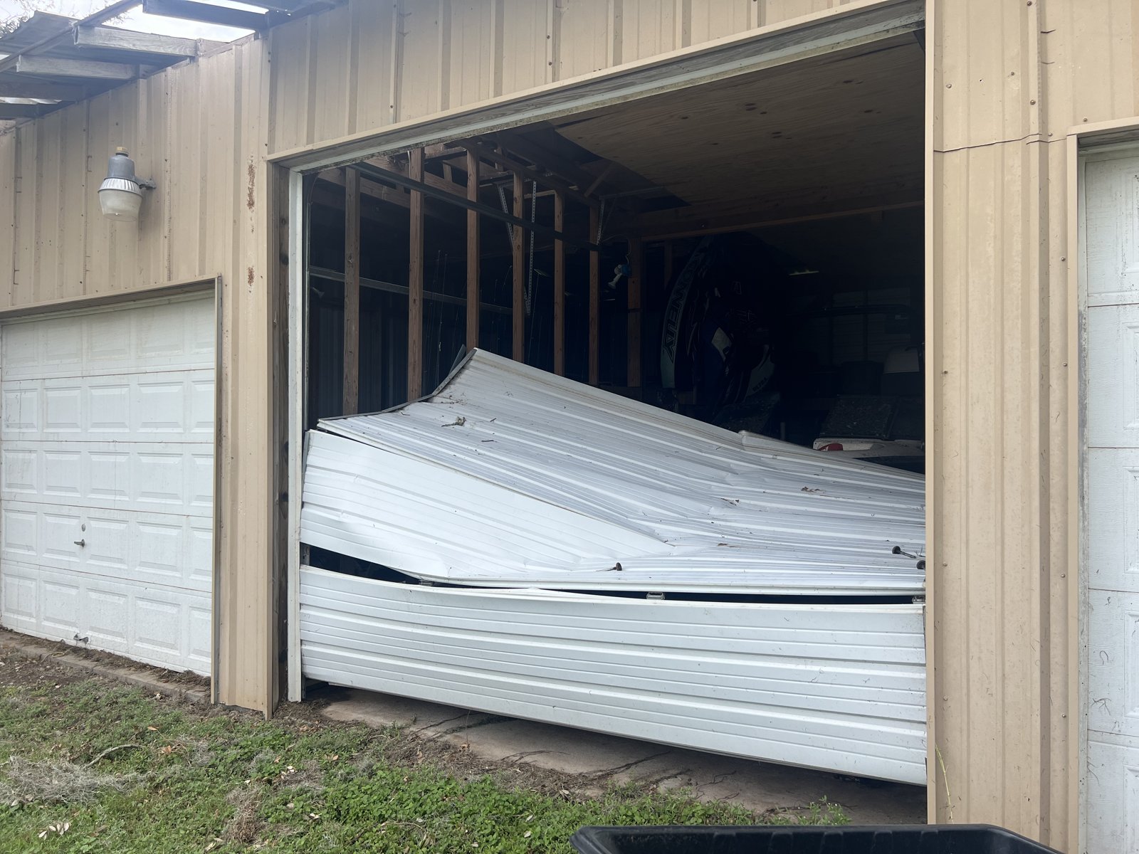 Storm-damaged garage door on a metal building Garage door panels crushed and bent inside a tan metal building after a storm