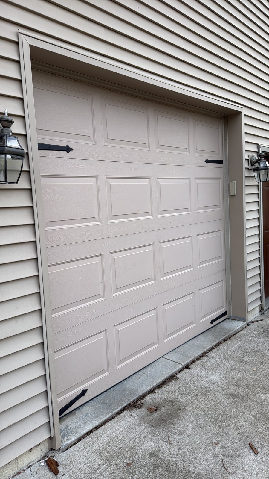 Raised-panel single garage door with black hardware Beige raised-panel single garage door with black decorative hinges and handles
