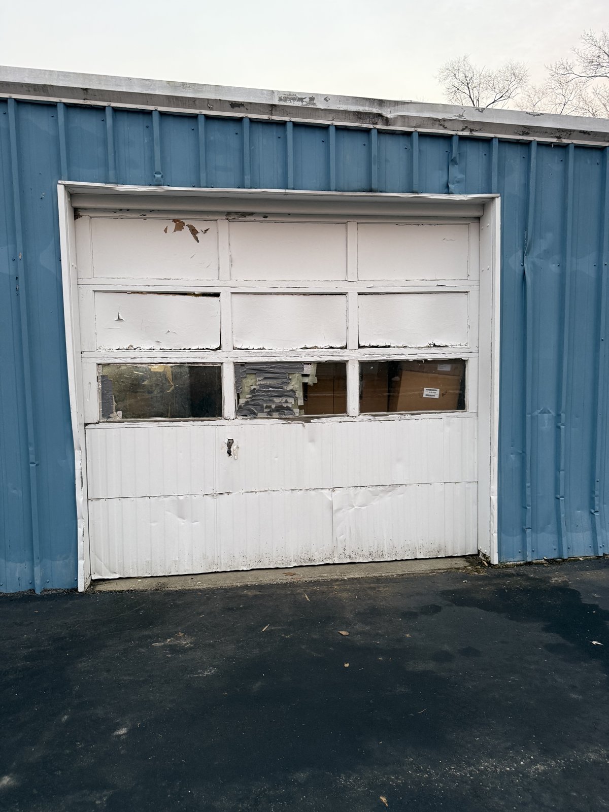 Worn commercial garage door before replacement Old damaged white commercial garage door on a blue metal building
