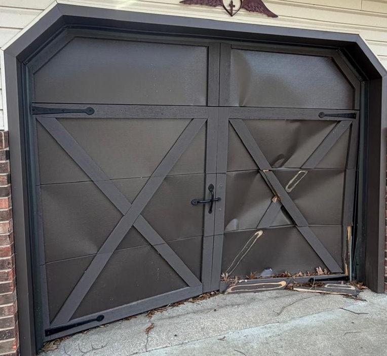 Damaged carriage-style garage door Close-up of a dark brown carriage-style garage door with dented panels and broken crossbuck trim
