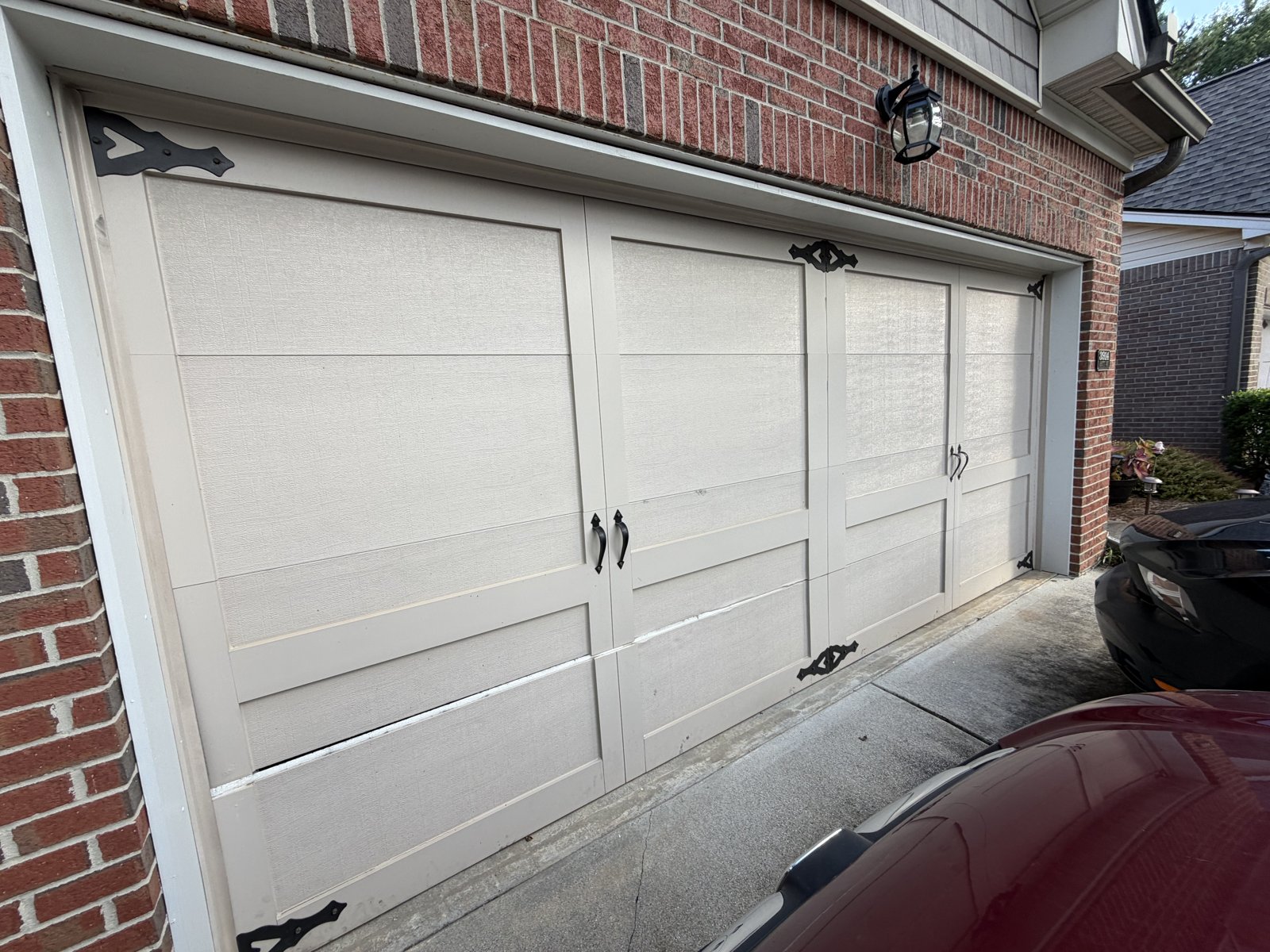 Wide white carriage double garage door Wide white carriage-style double garage door with black hardware on a brick home