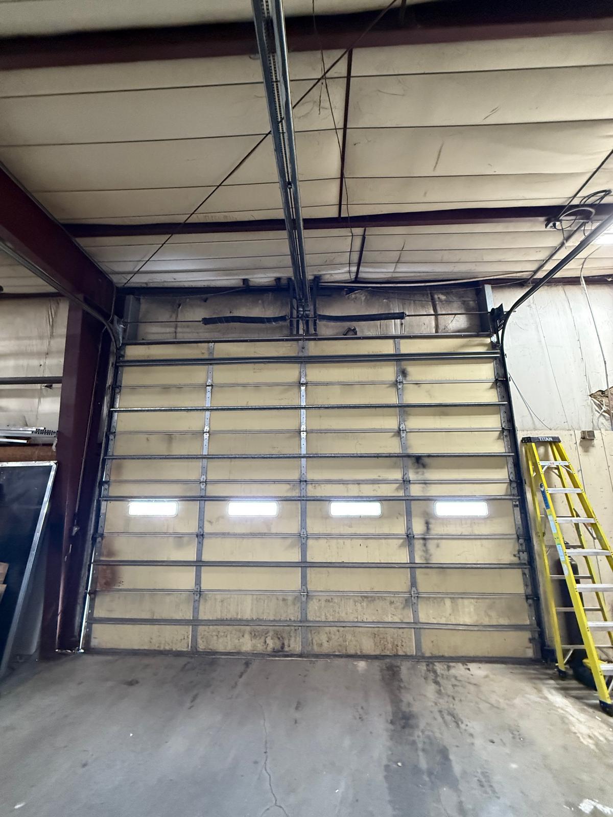 Commercial insulated garage door repair in Roswell, GA Large insulated commercial garage door inside a warehouse bay during repair in Roswell, GA