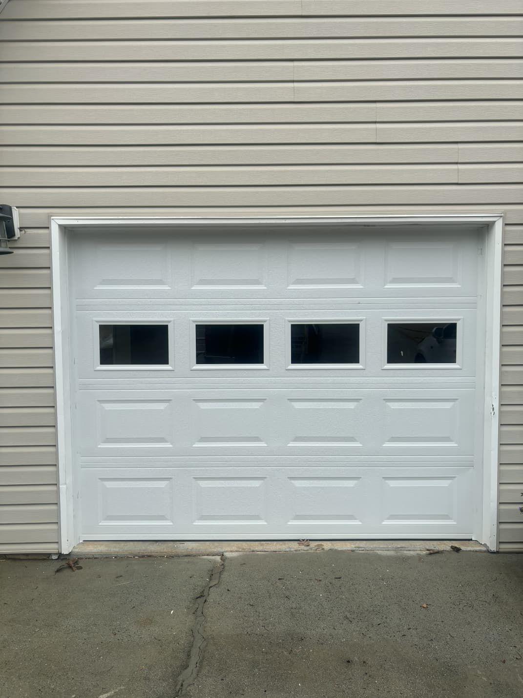 Single-car garage door replacement in Acworth, GA New white single-car garage door with window row installed on a vinyl-sided home in Acworth, GA