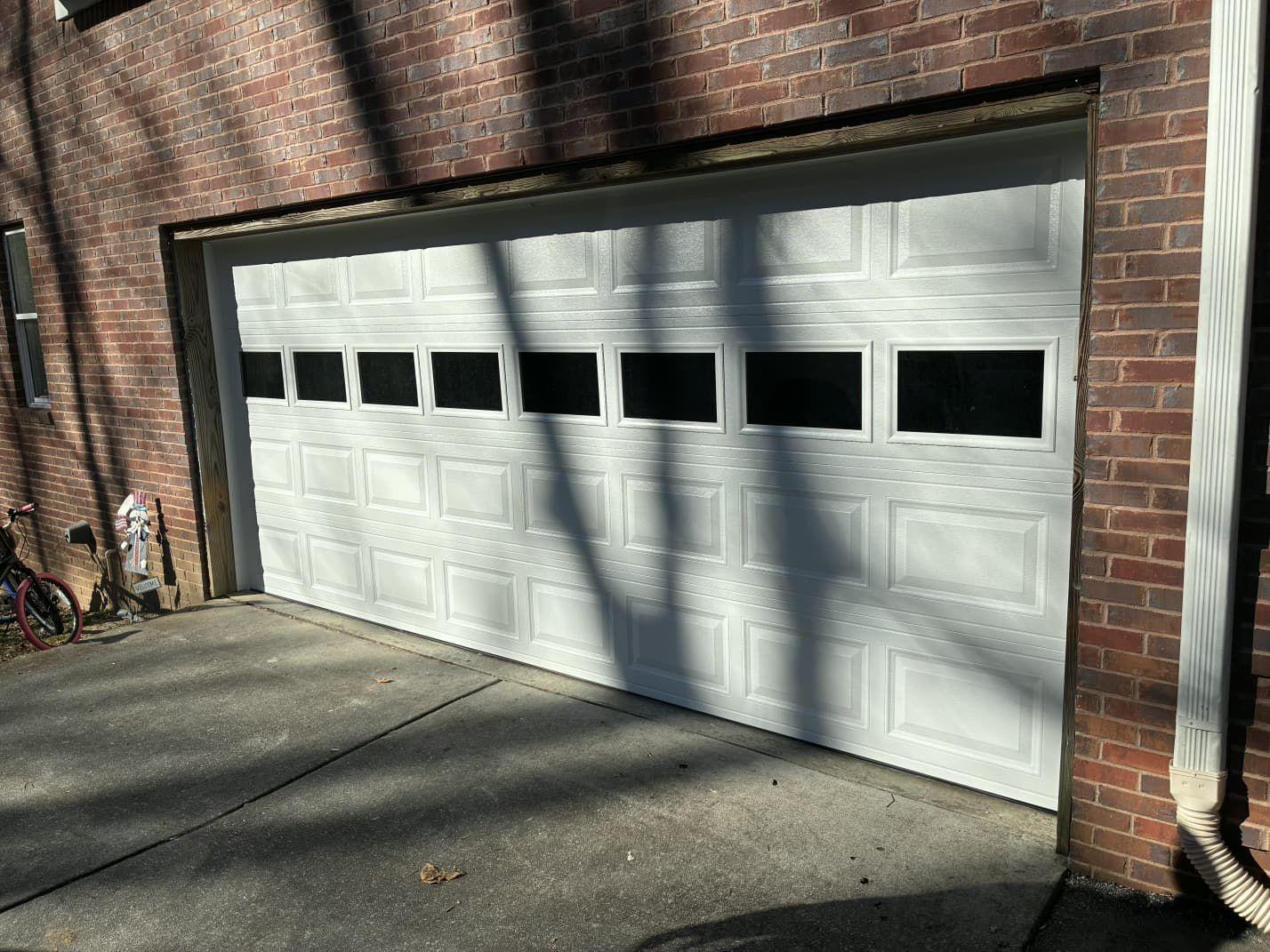 New white panel garage door installation in Canton, GA Newly installed white raised-panel garage door with window inserts on a brick home in Canton, GA